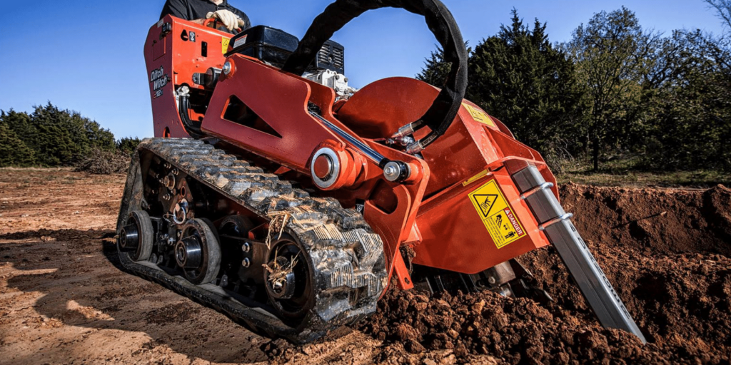 Red trencher machine digging into the ground at a construction site
